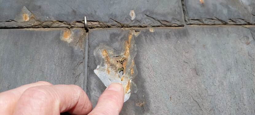 Klaas Schoots met zijn vinger bij een gat in een lei door oxidatie van minerale sporen