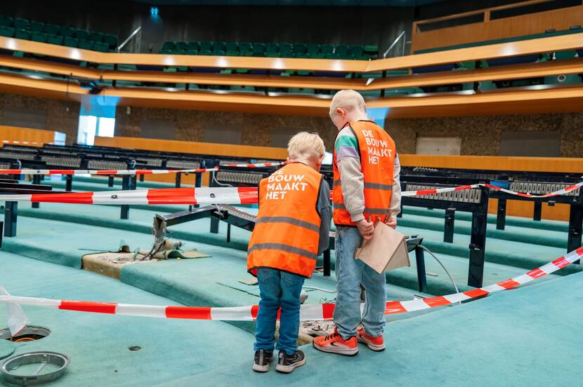 Twee jonge bezoekers kijken naar onttakeld bankje in de plenaire zaal Tweede Kamer op Dag van de Bouw Binnenhof 2024