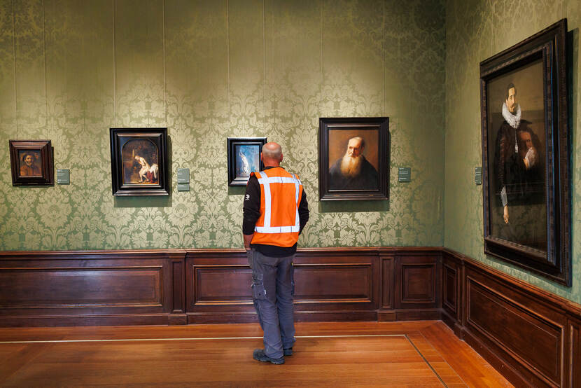 Bouwmedewerker in rood hesje bekijkt werken van Rembrandt