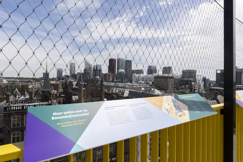 Informatiebord op het bovenste platform van het uitzichtpunt met op de achtergrond Ridderzaal en de skyline van Den Haag